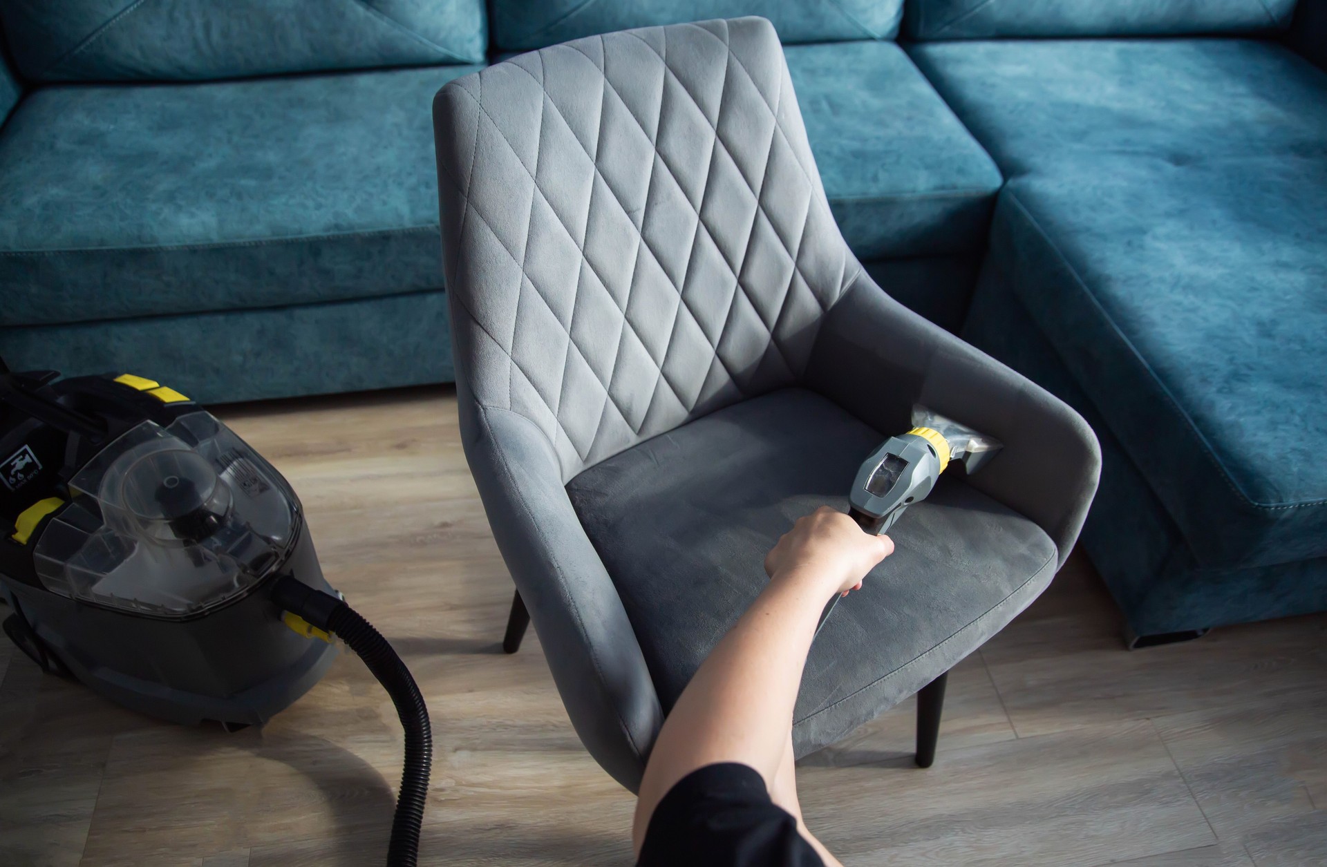 The hands of a girl with a washing vacuum cleaner clean and wash the gray upholstery of a soft chair from dirt. Cleaning services, business, close-up. Copy space for text